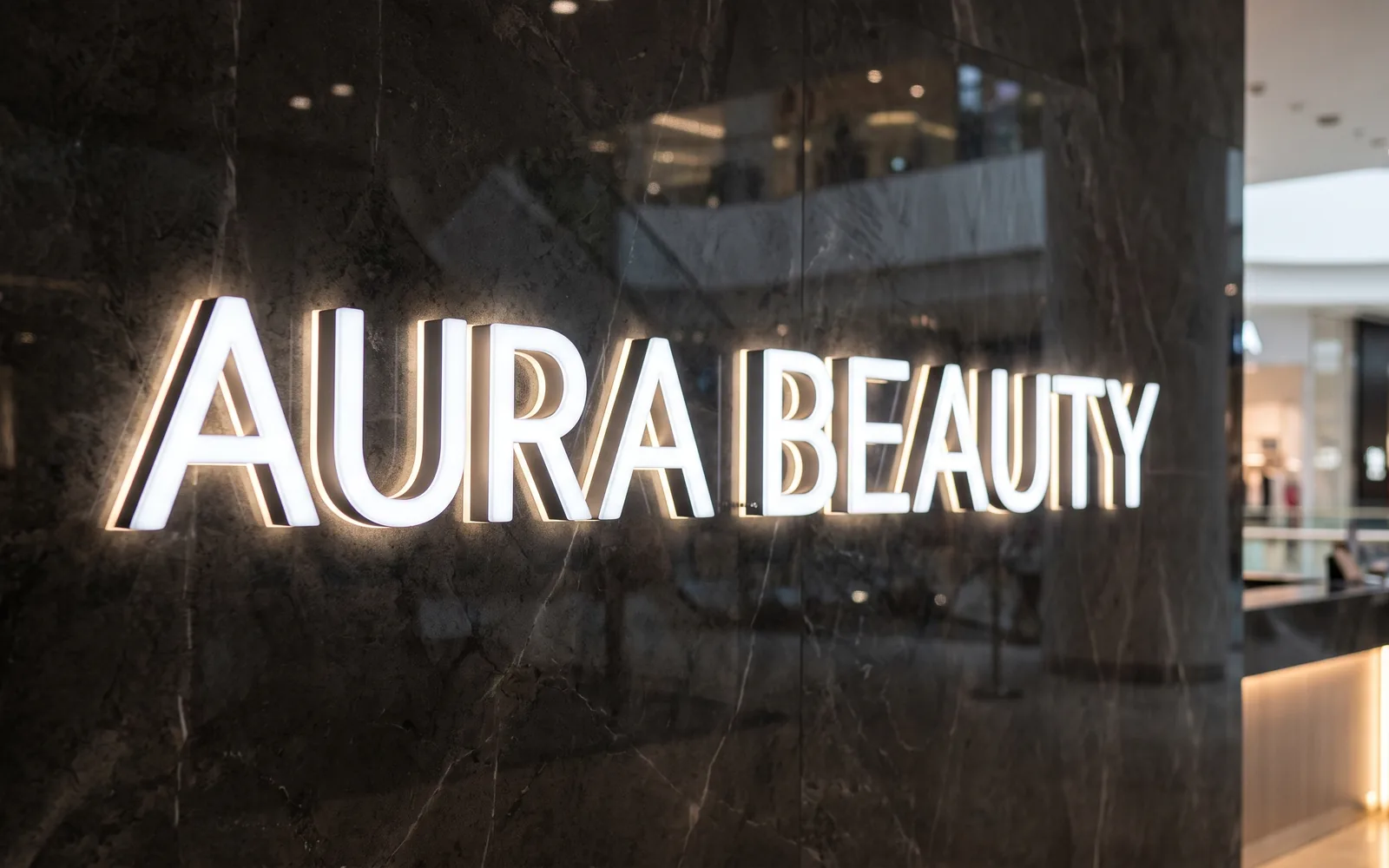 Design rendering: front and back lit acrylic letters glowing on a dark marble wall in a shopping mall